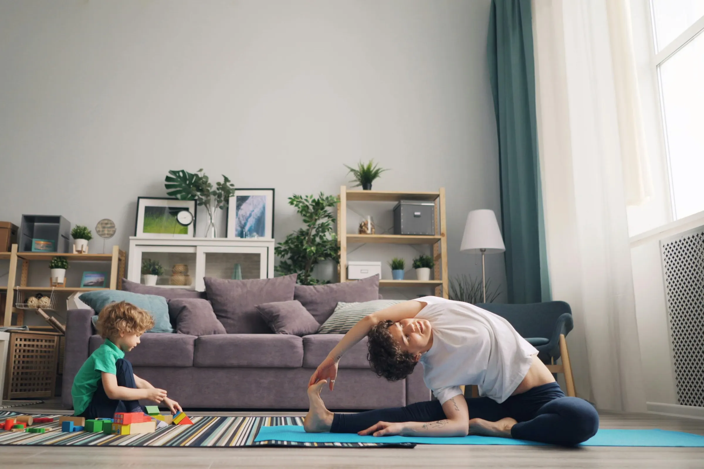 A parent stretches in the living room while their child plays nearby