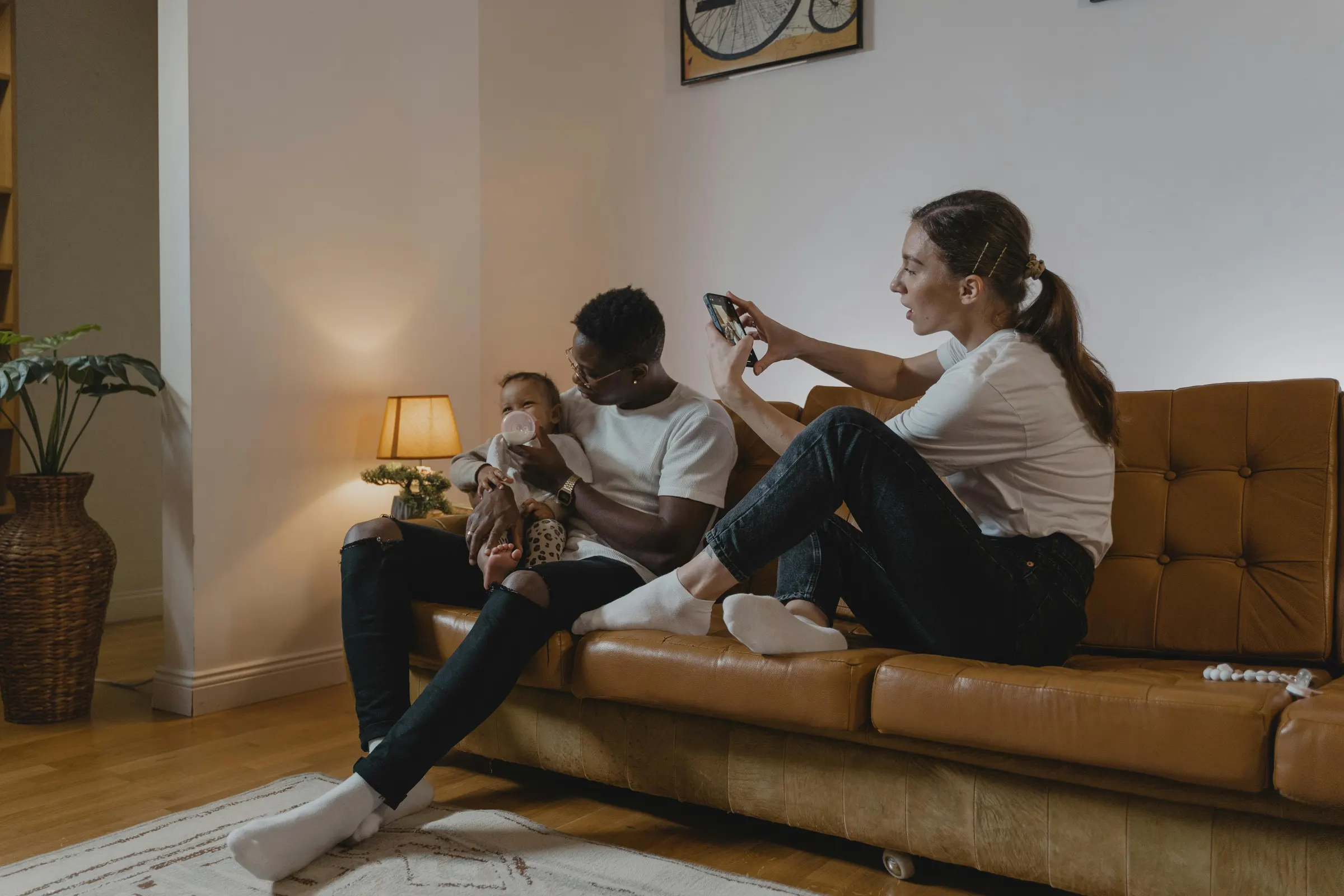 A family on the couch — one parent feeding a baby, the other on a phone